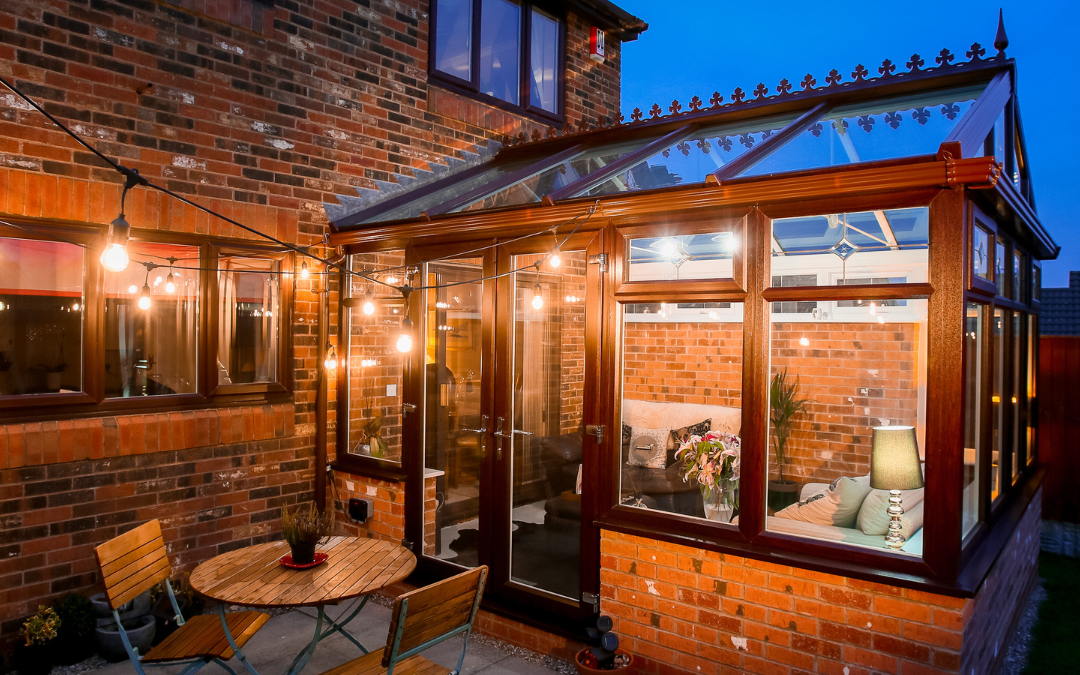 Night-time conservatory exterior with a red brown wood and brick colour scheme - side view point